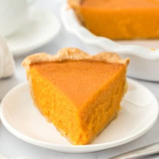 A slice of homemade sweet potato pie on a white plate ready to serve with pie in the background