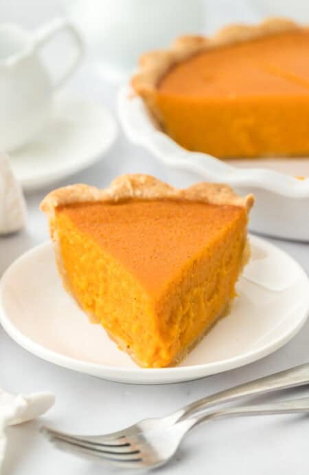 A slice of homemade sweet potato pie on a white plate ready to serve with pie in the background