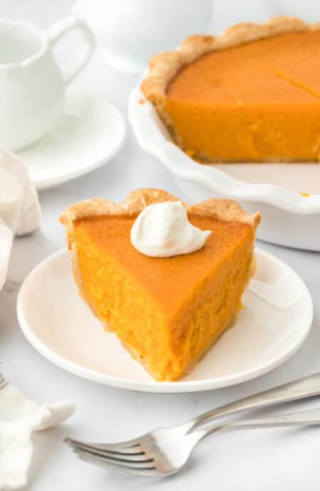 A slice of Southern sweet potato pie recipe on a white plate with full pie in the white background