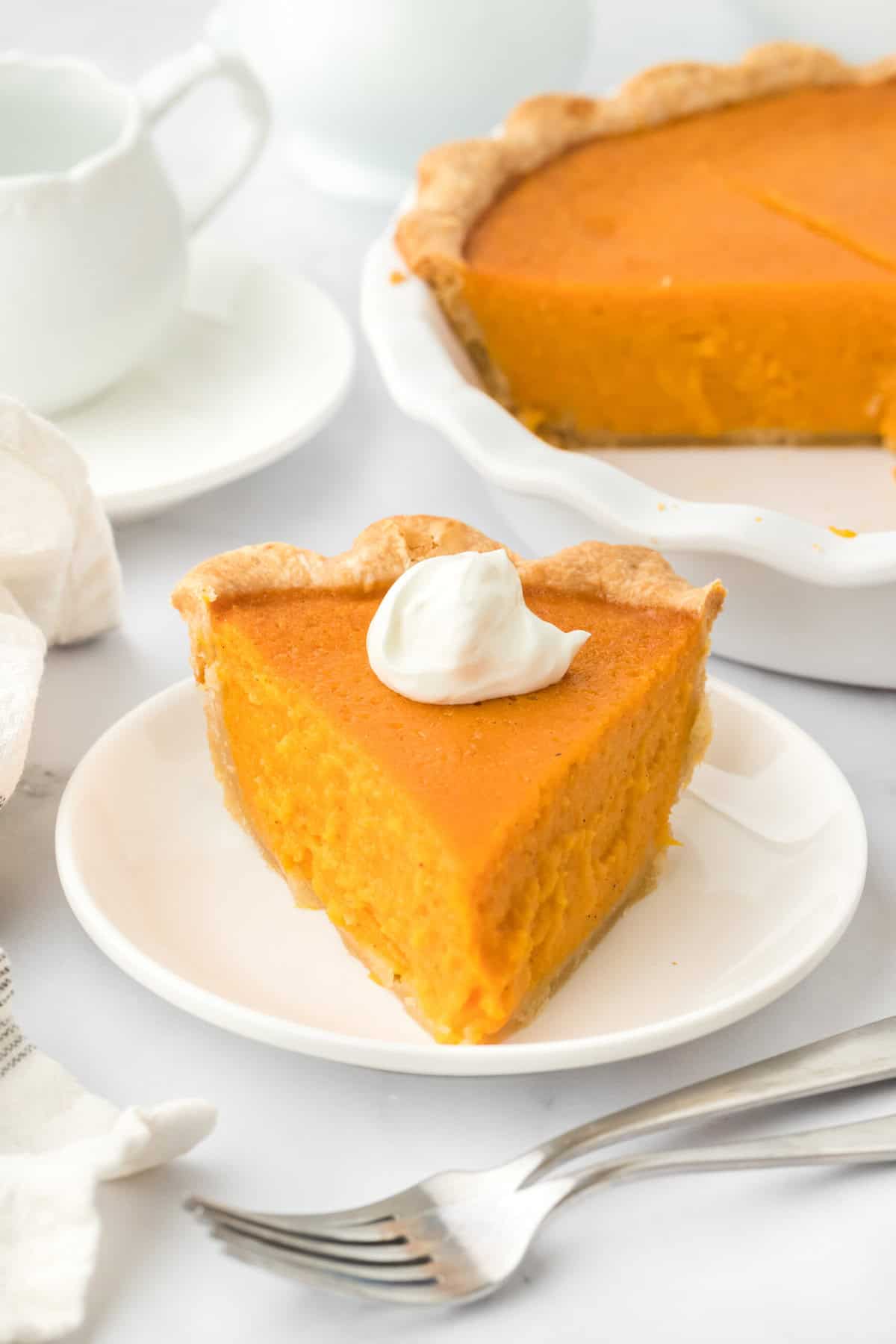 A slice of Southern sweet potato pie recipe on a white plate with full pie in the white background