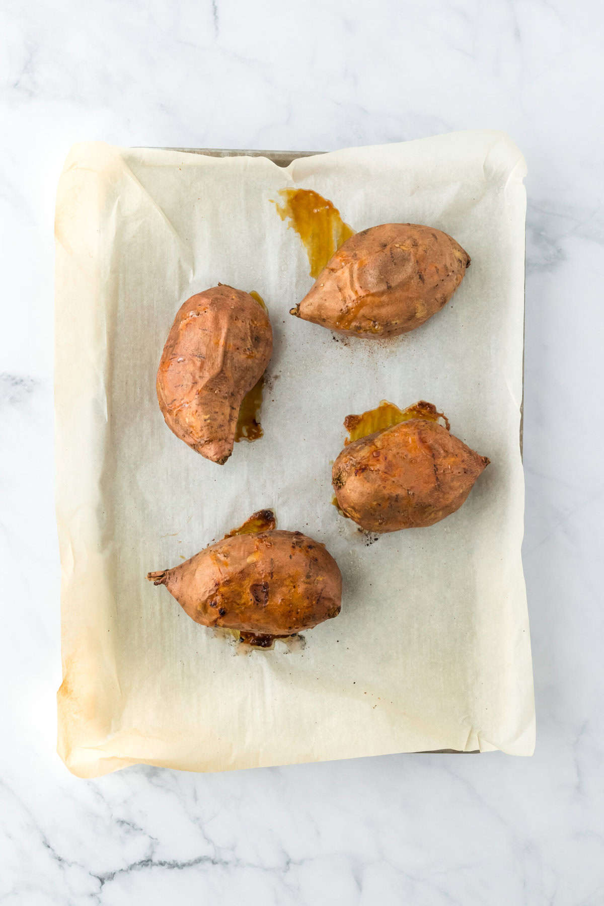 Baked sweet potatoes on a parchment lined baking sheet.