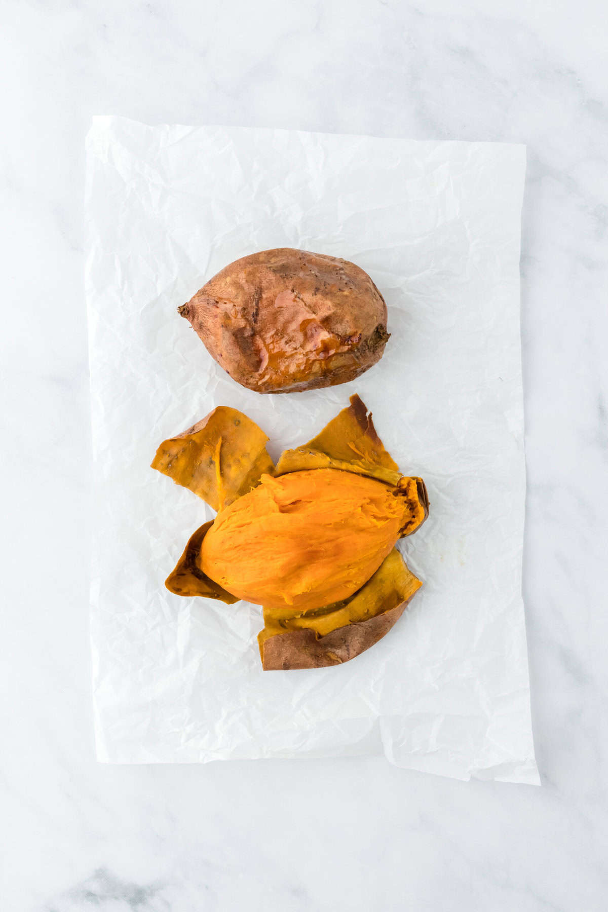 Baked sweet potatoes being peeled on a white countertop