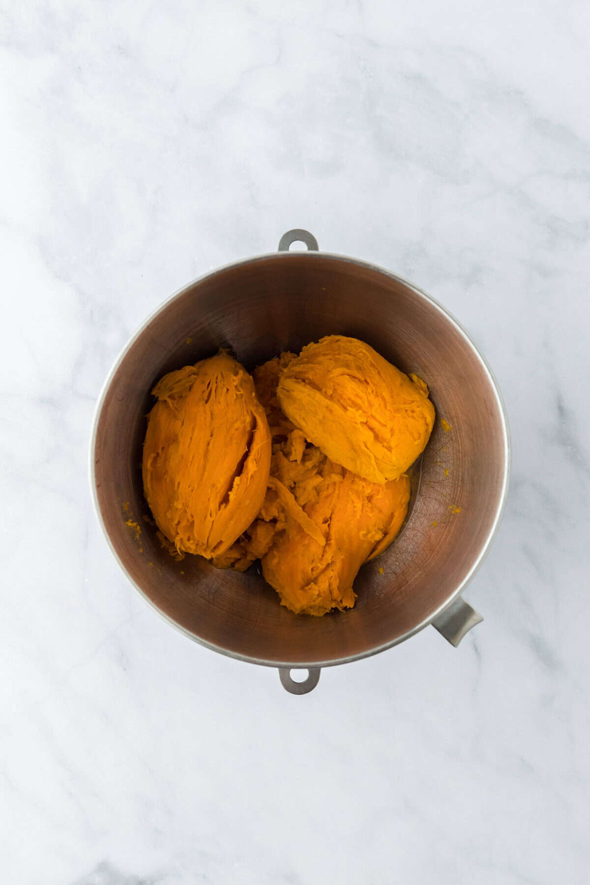 Baked sweet potatoes in a mixer bowl on white countertop