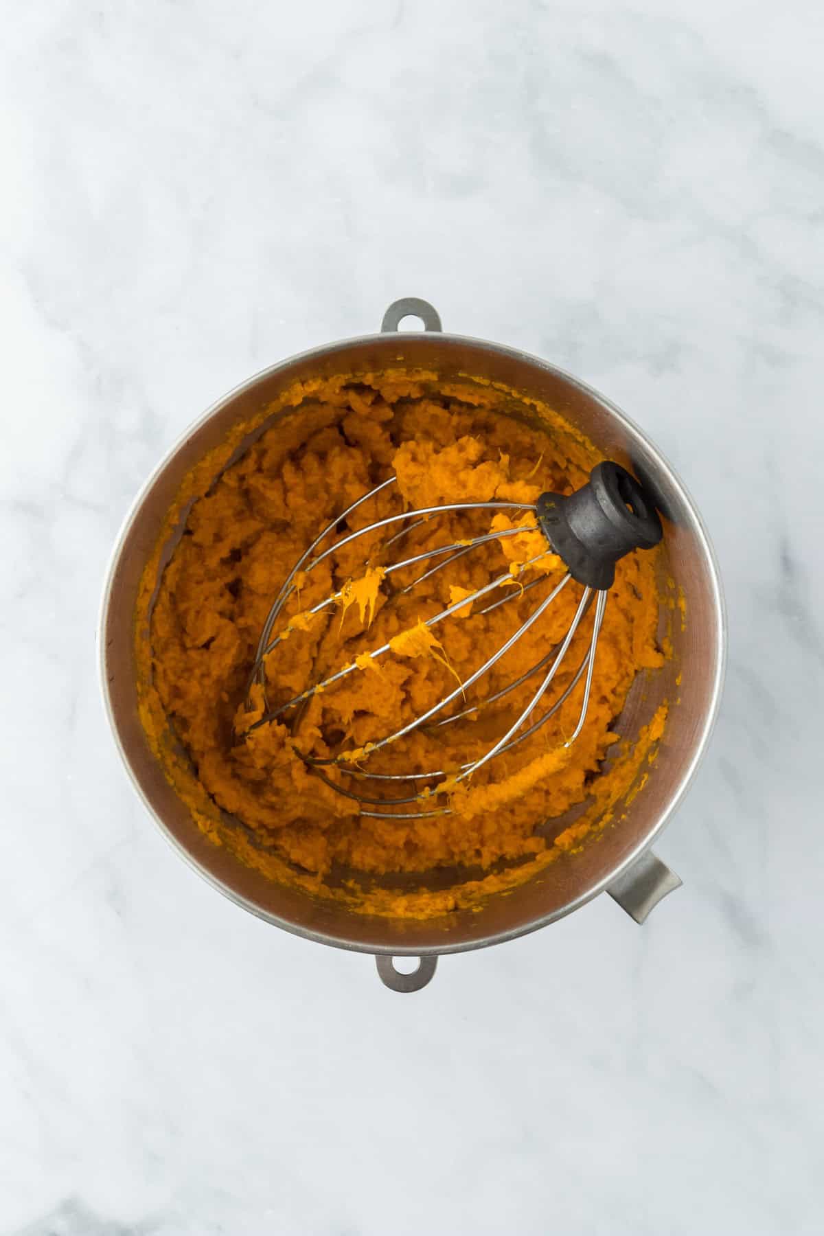 Mixed sweet potato filling in a stand mixer bowl with whisk attachment on white countertop