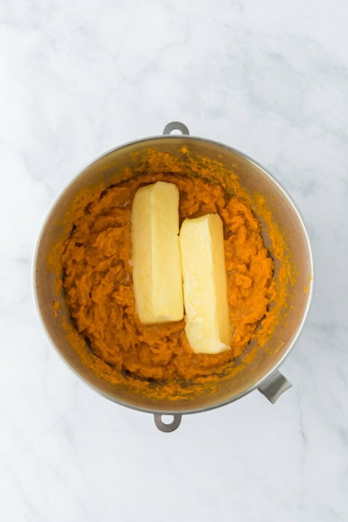 Butter added to mixed sweet potato filling in stand mixer bowl on white countertop