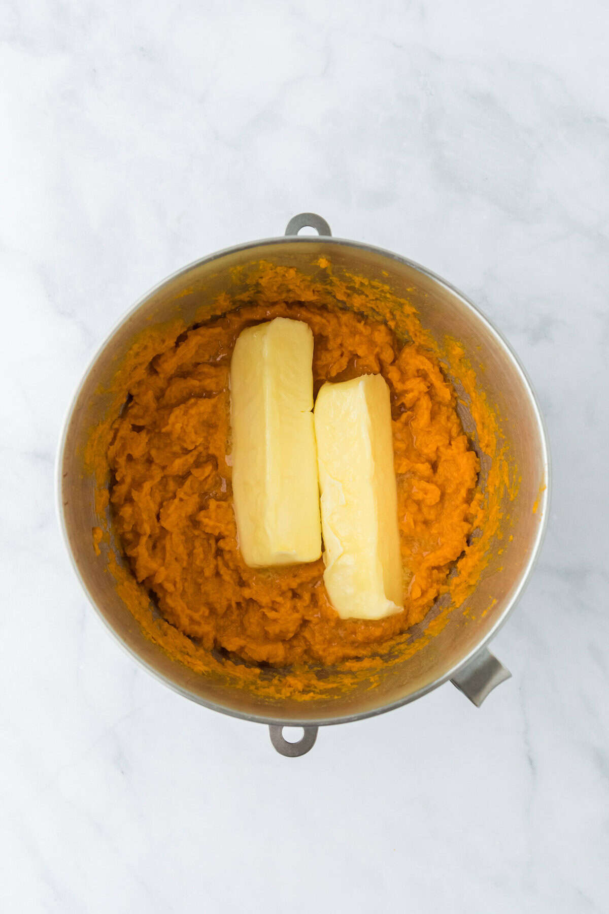 Butter added to mixed sweet potato filling in stand mixer bowl on white countertop