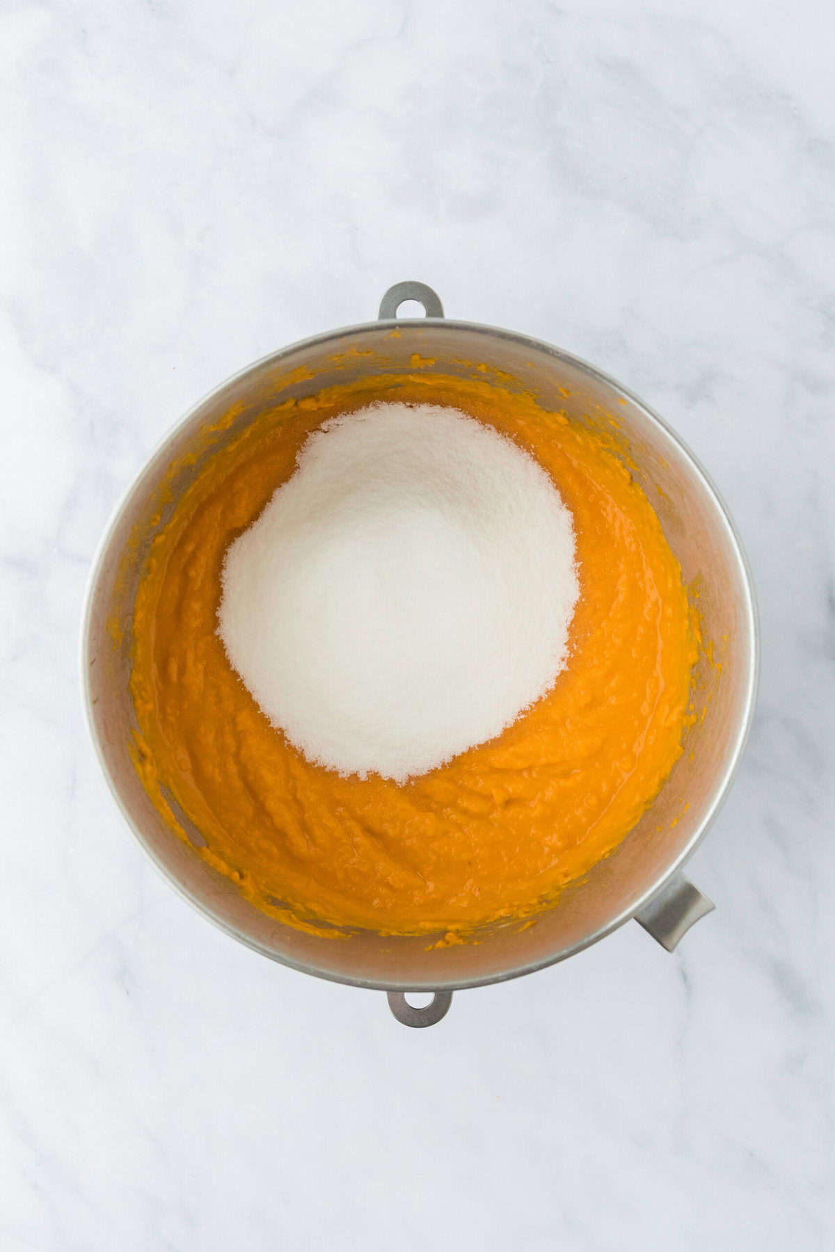 Granulated sugar added to sweet potato pie filling in a stand mixer bowl on white background