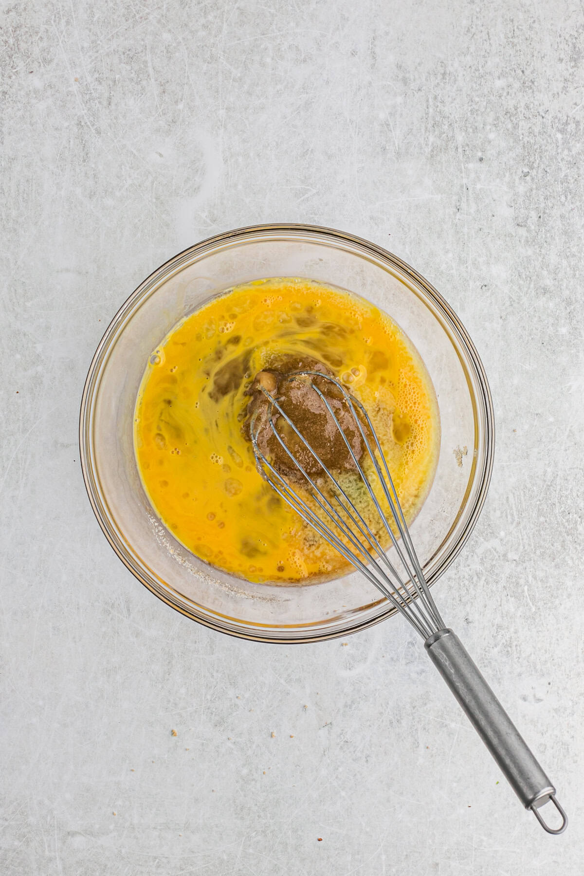 Eggs and brown sugar being whisked together in a glass bowl