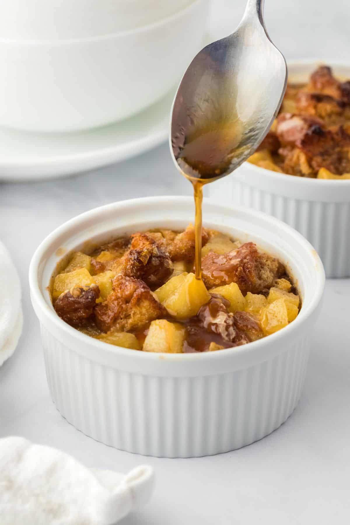  A spoon drizzling syrup over a ramekin filled with apple fritter bread pudding