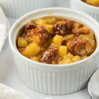 Closeup of a small ramekin filled with golden-brown apple fritter bread pudding with more ramekins in the background.