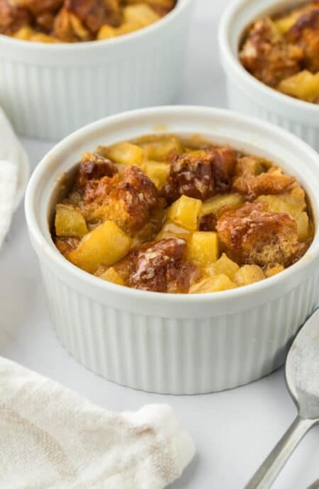 Closeup of a small ramekin filled with golden-brown apple fritter bread pudding with more ramekins in the background.