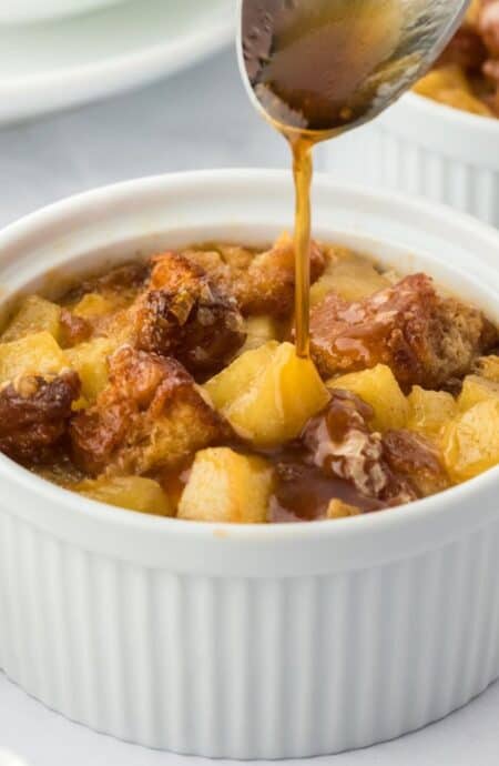 A spoon drizzling syrup over a ramekin filled with apple fritter bread pudding