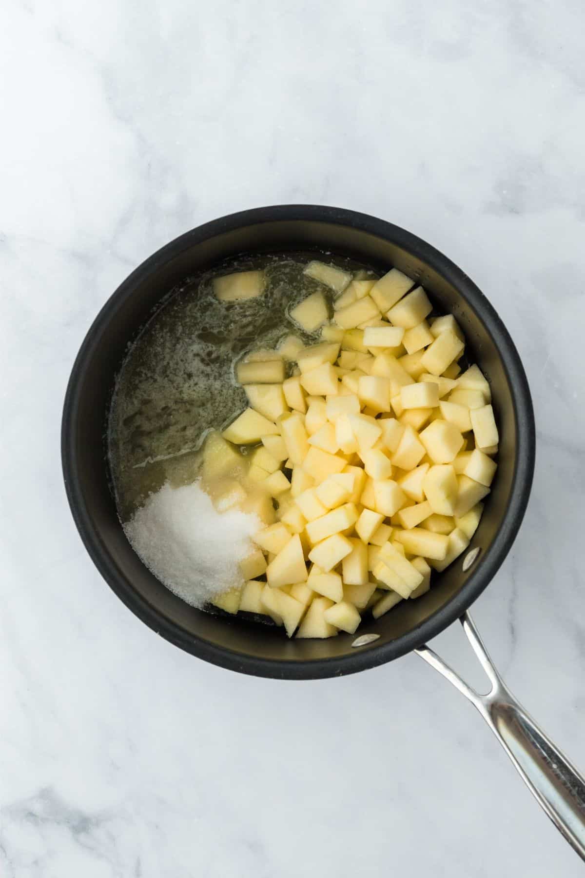 Closeup of diced apples in a saucepan with sugar, cooking in liquid.