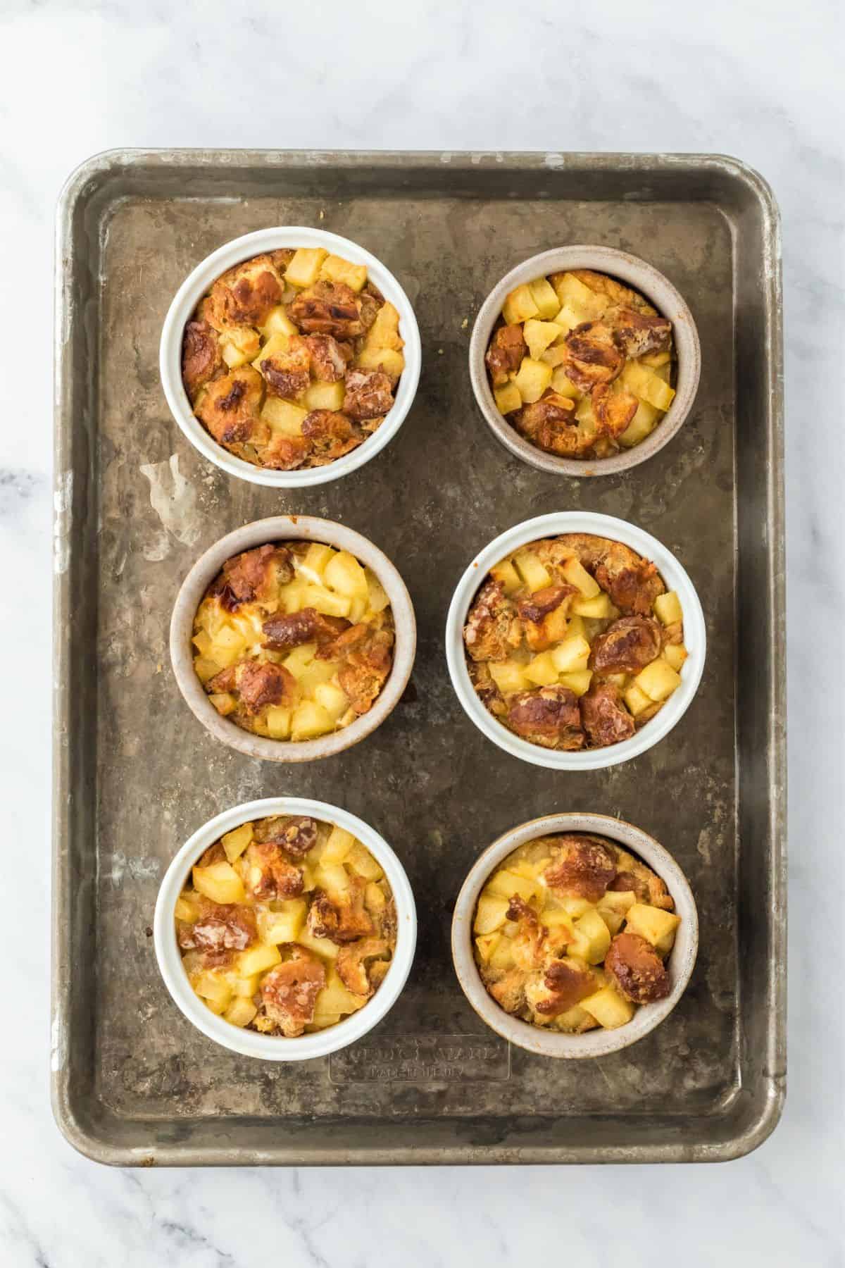 Baked apple fritter bread pudding in ramekins, golden and slightly crisp on top.