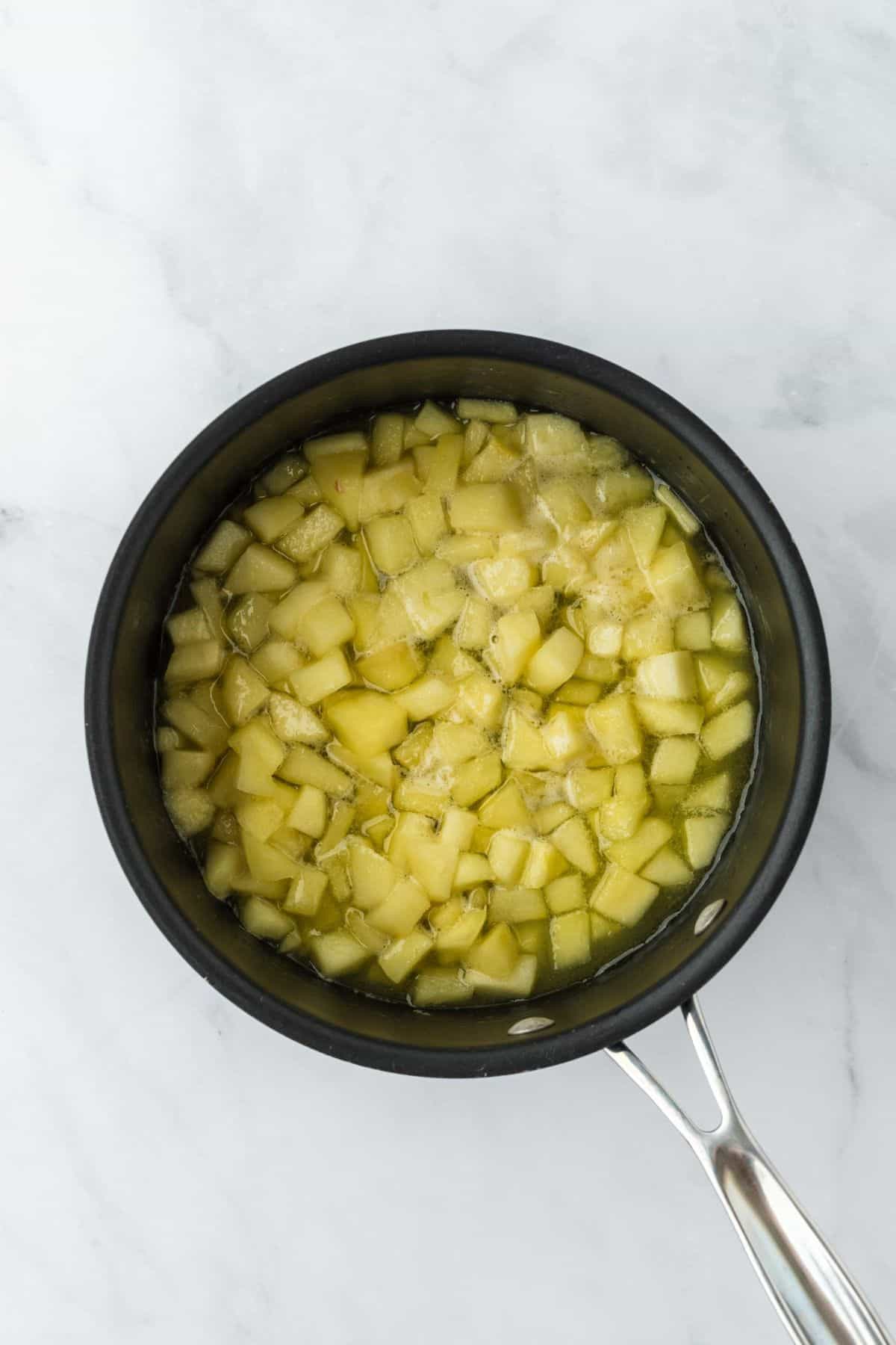 Cooked diced apples simmering in liquid in a saucepan.