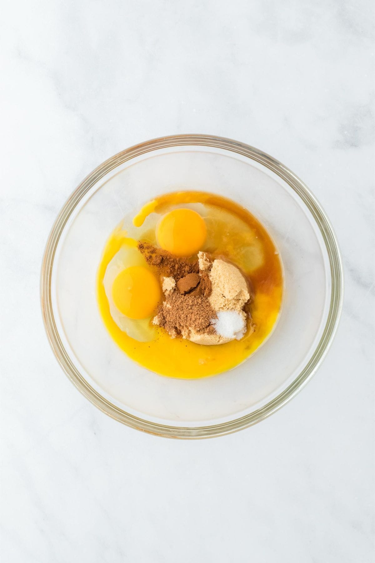 Eggs, sugar, and spices in a clear bowl, ready to be mixed.