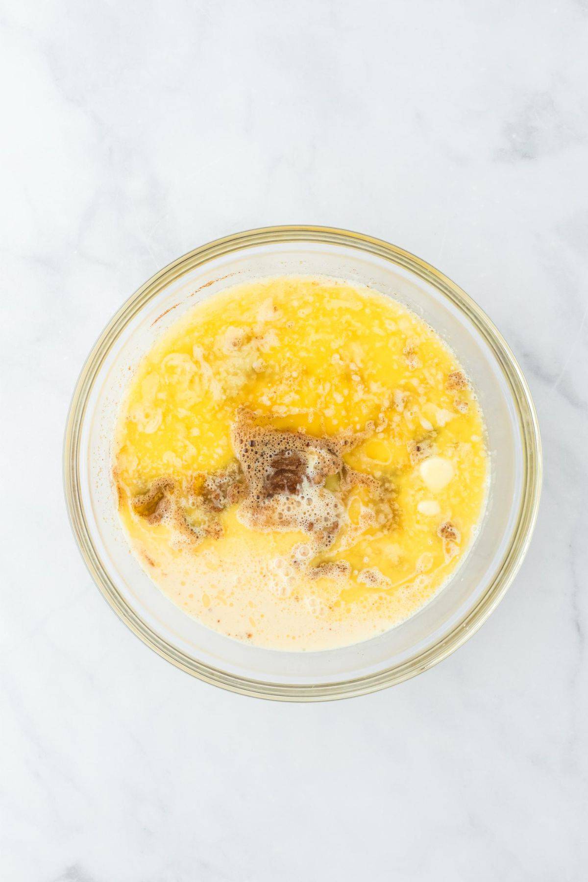 Egg mixture combined with melted butter and evaporated milk in a clear bowl.