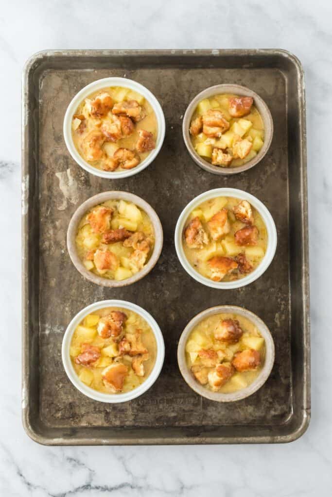 Ramekins filled with bread, apples, and custard mixture.