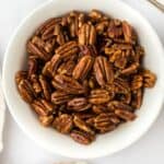 Candied pecans in a white bowl with brown sugar on a spoon