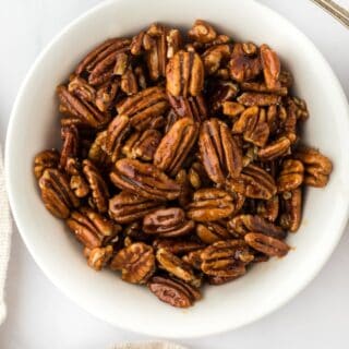 Candied pecans in a white bowl with brown sugar on a spoon