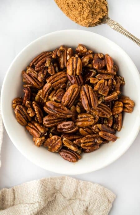 Candied pecans in a white bowl with brown sugar on a spoon