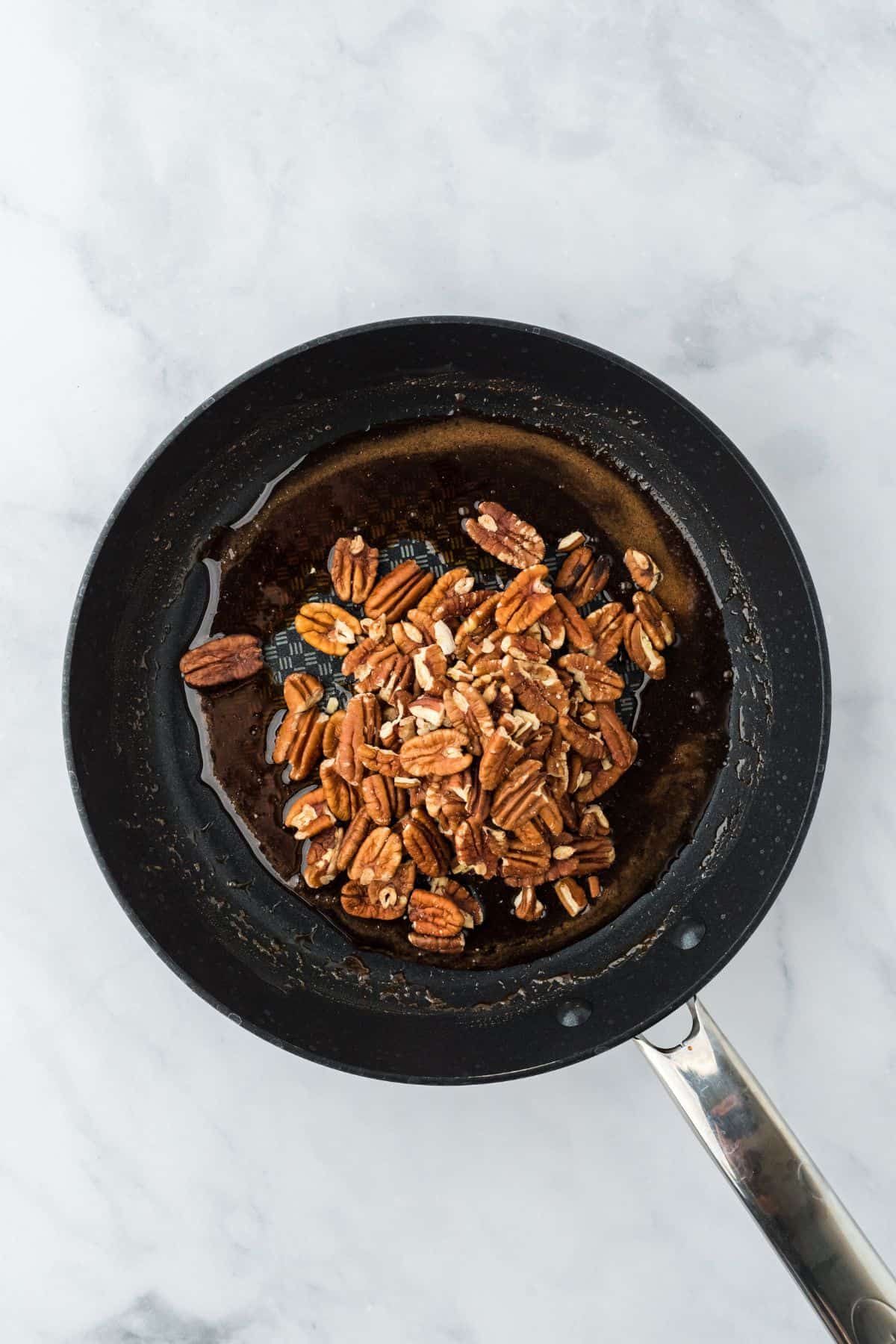 Pecans added to the caramel-like liquid in the frying pan