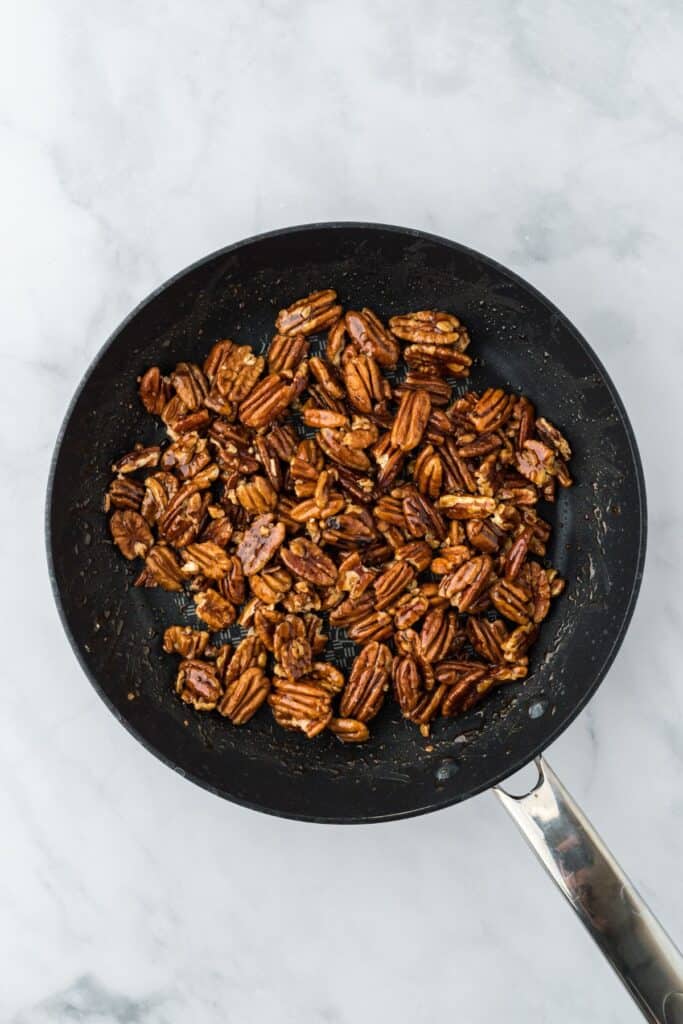 Pecans fully coated in the caramel mixture, still in the frying pan