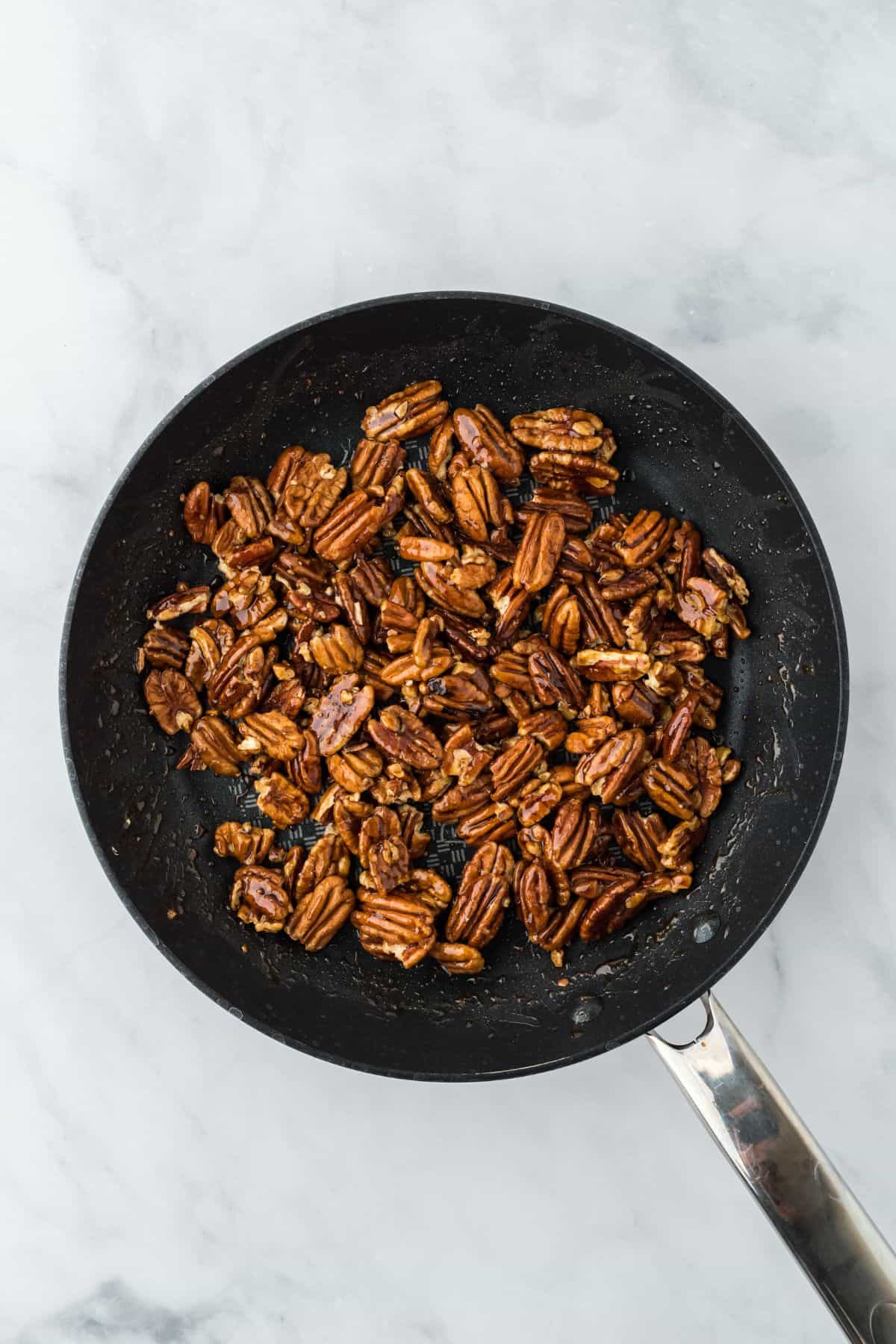 Pecans fully coated in the caramel mixture, still in the frying pan