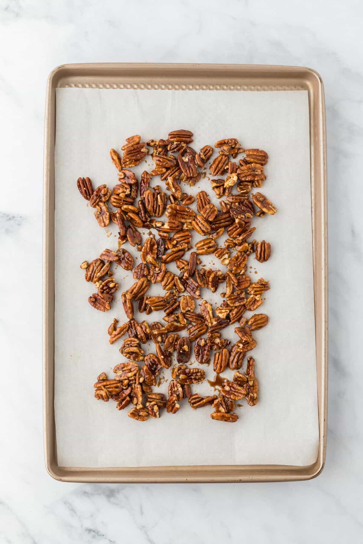 Caramel-coated pecans spread out on a parchment-lined baking sheet