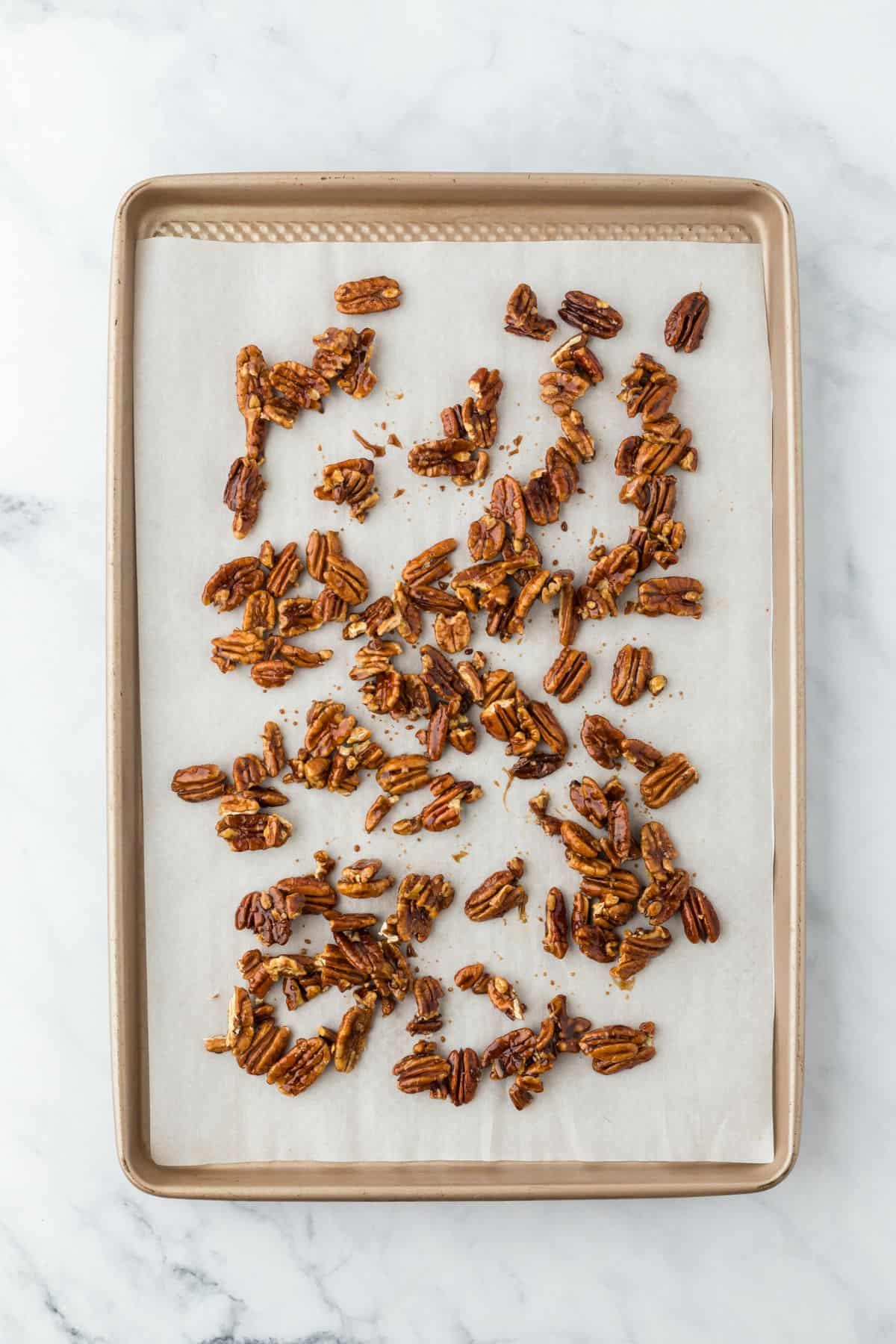 Candied pecans spaced out on the same baking sheet after cooling