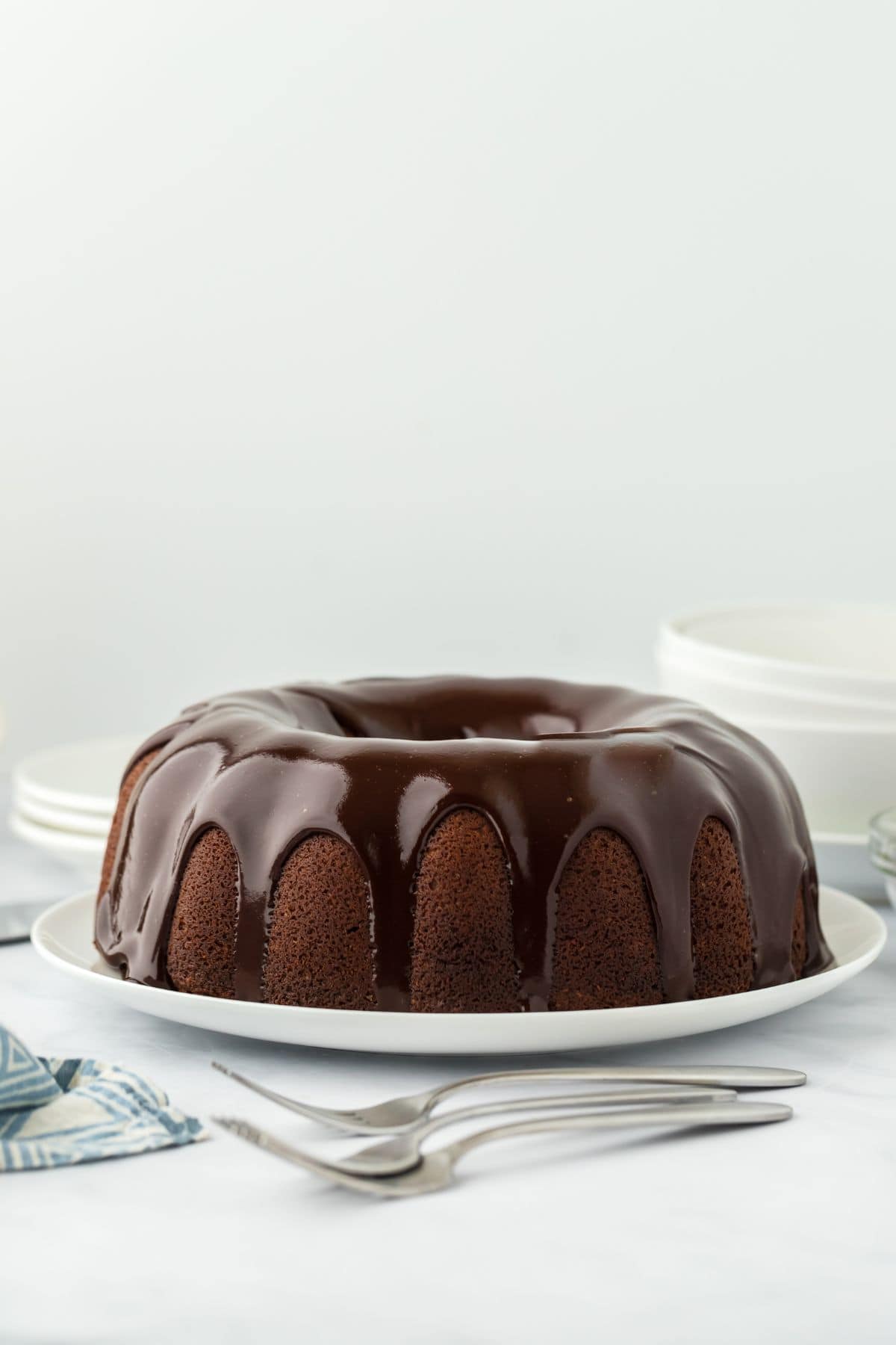 A whole chocolate pound cake covered in chocolate glaze, resting on a white plate with forks nearby