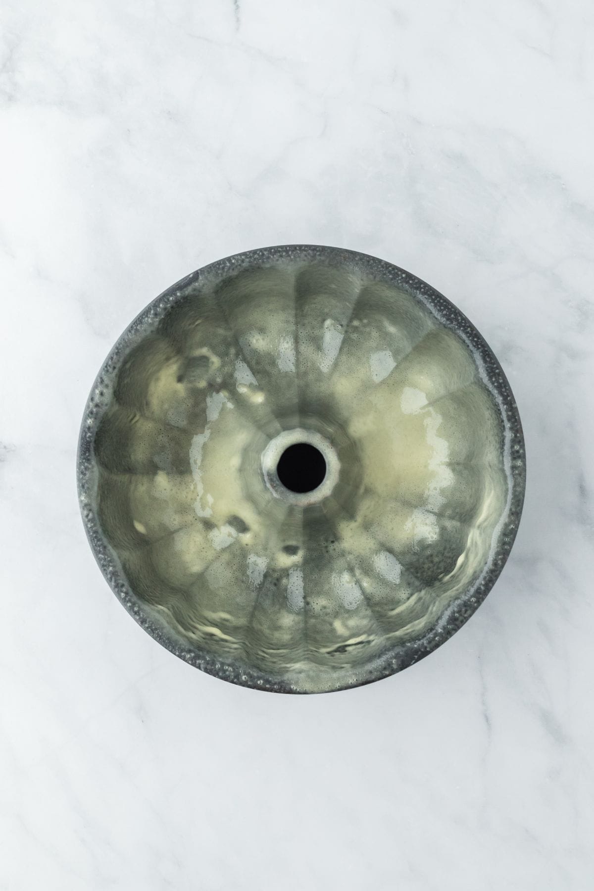 An overhead shot of a greased bundt pan on a marble surface