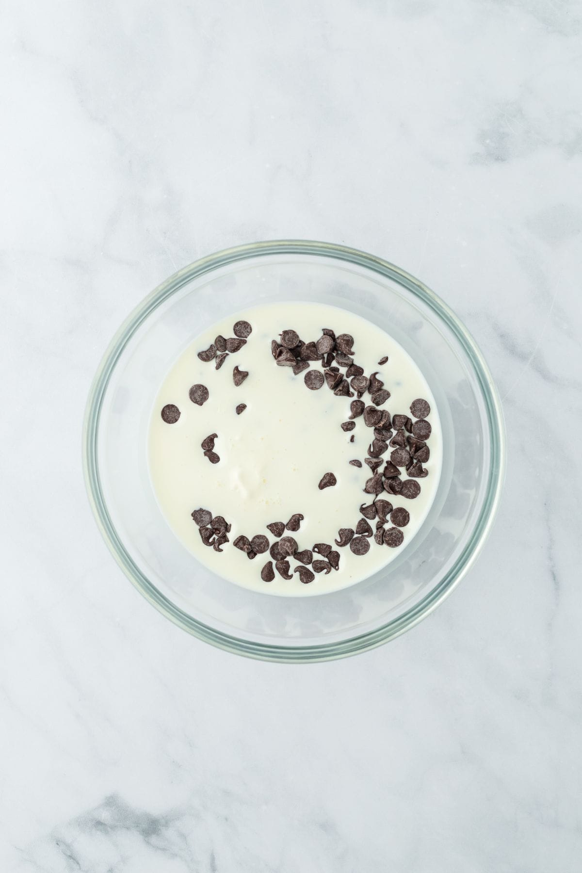 A bowl of cream and chocolate chips, ready to be melted for a glaze