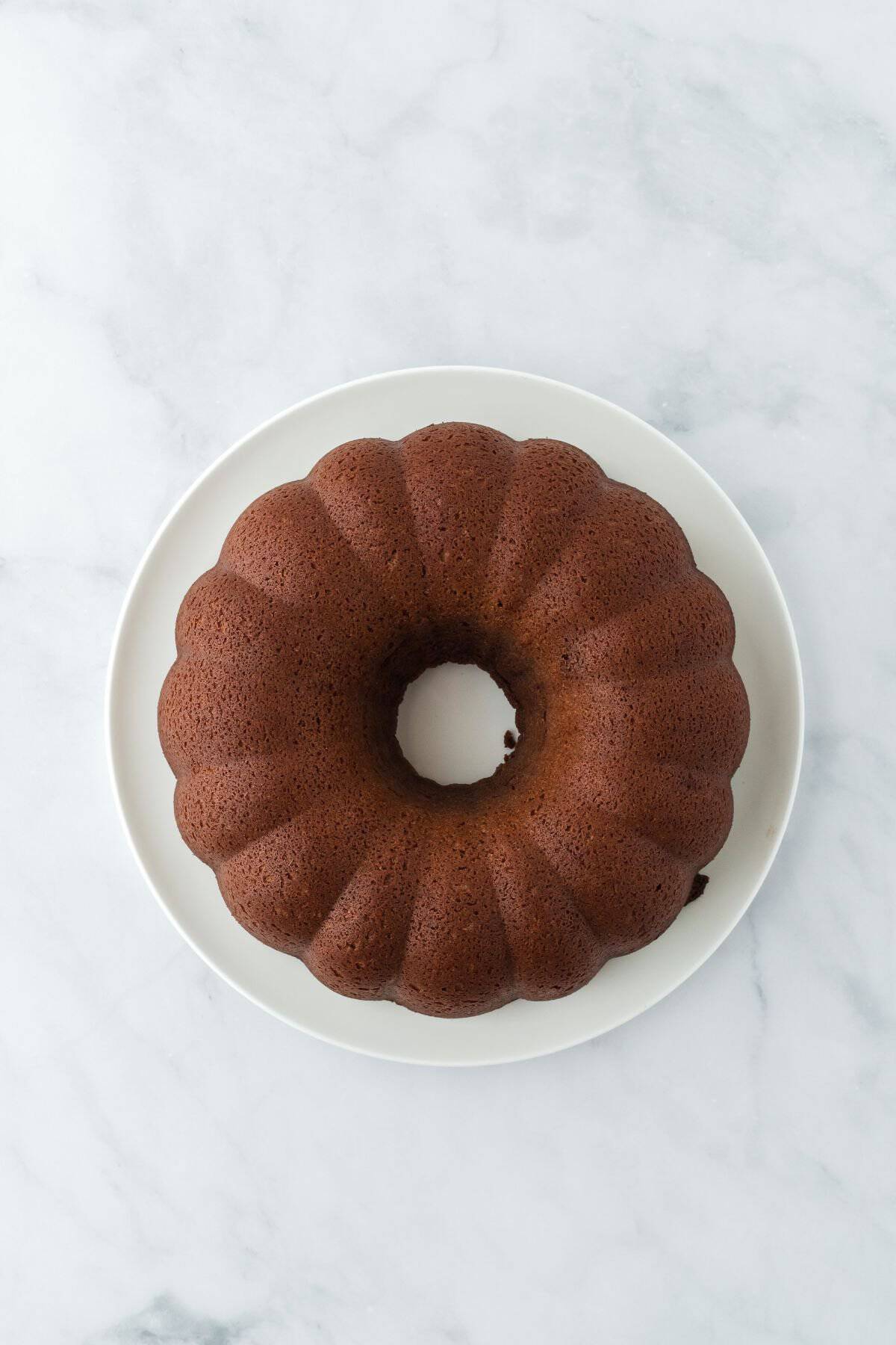 A plain chocolate pound cake on a white plate, before the glaze is added