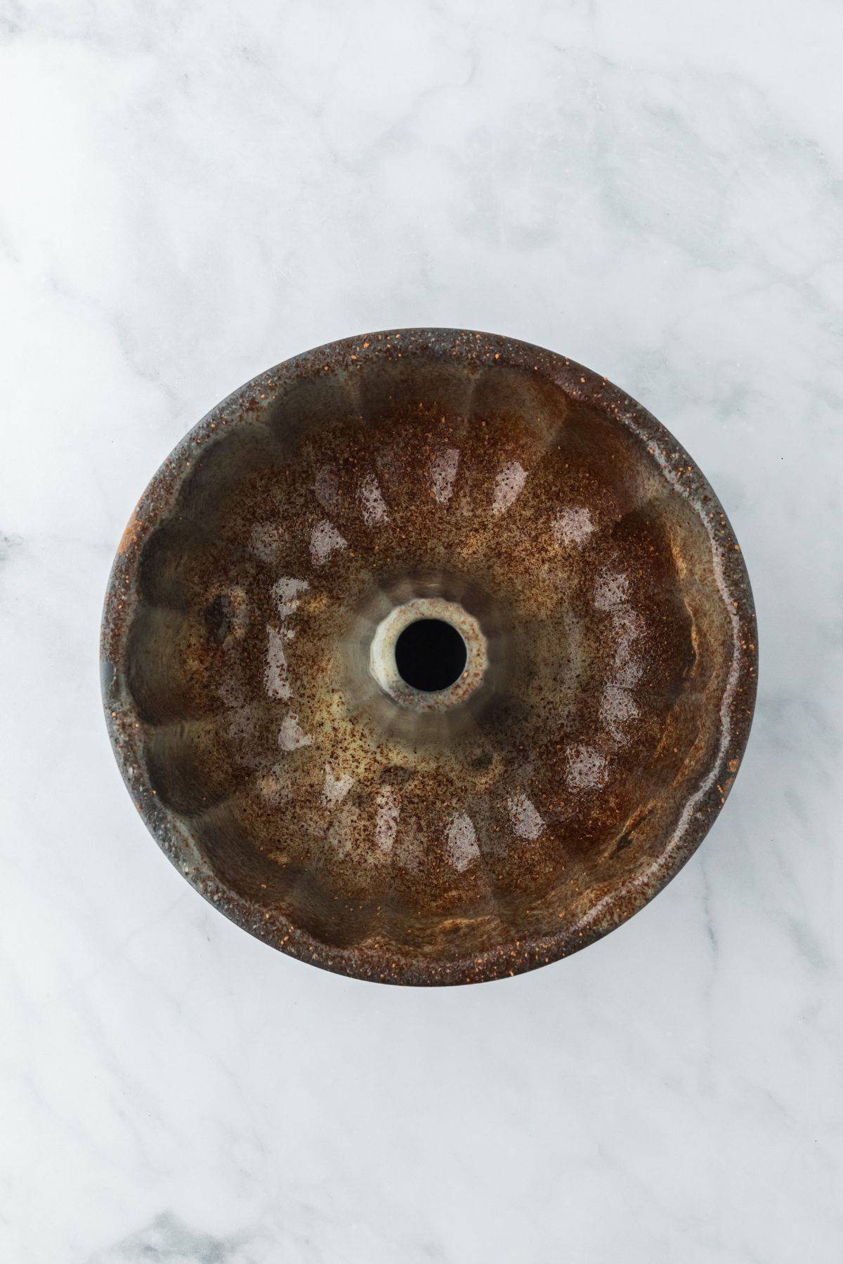 An overhead view of a bundt pan dusted with cocoa powder on a marble surface