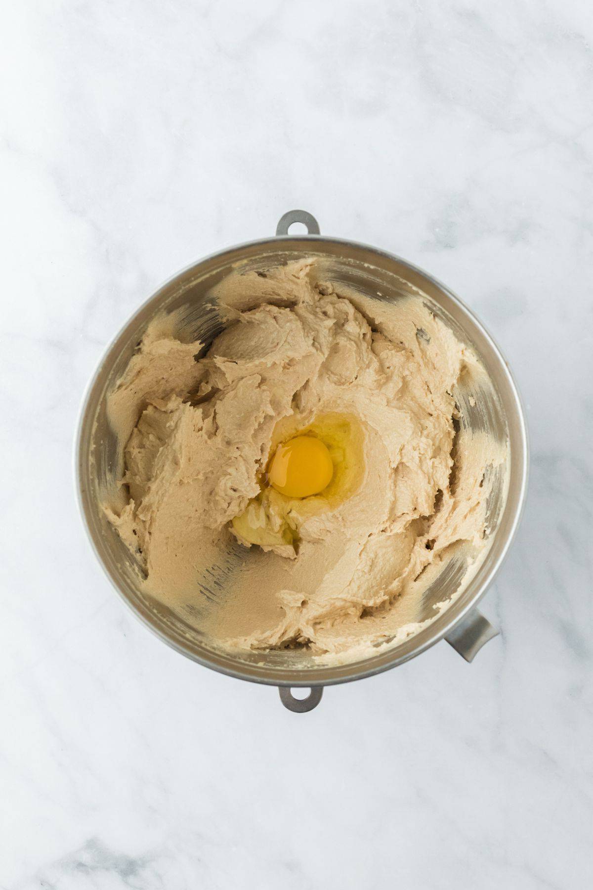 Creamed butter and sugar with an egg cracked into the center, in a metal mixing bowl