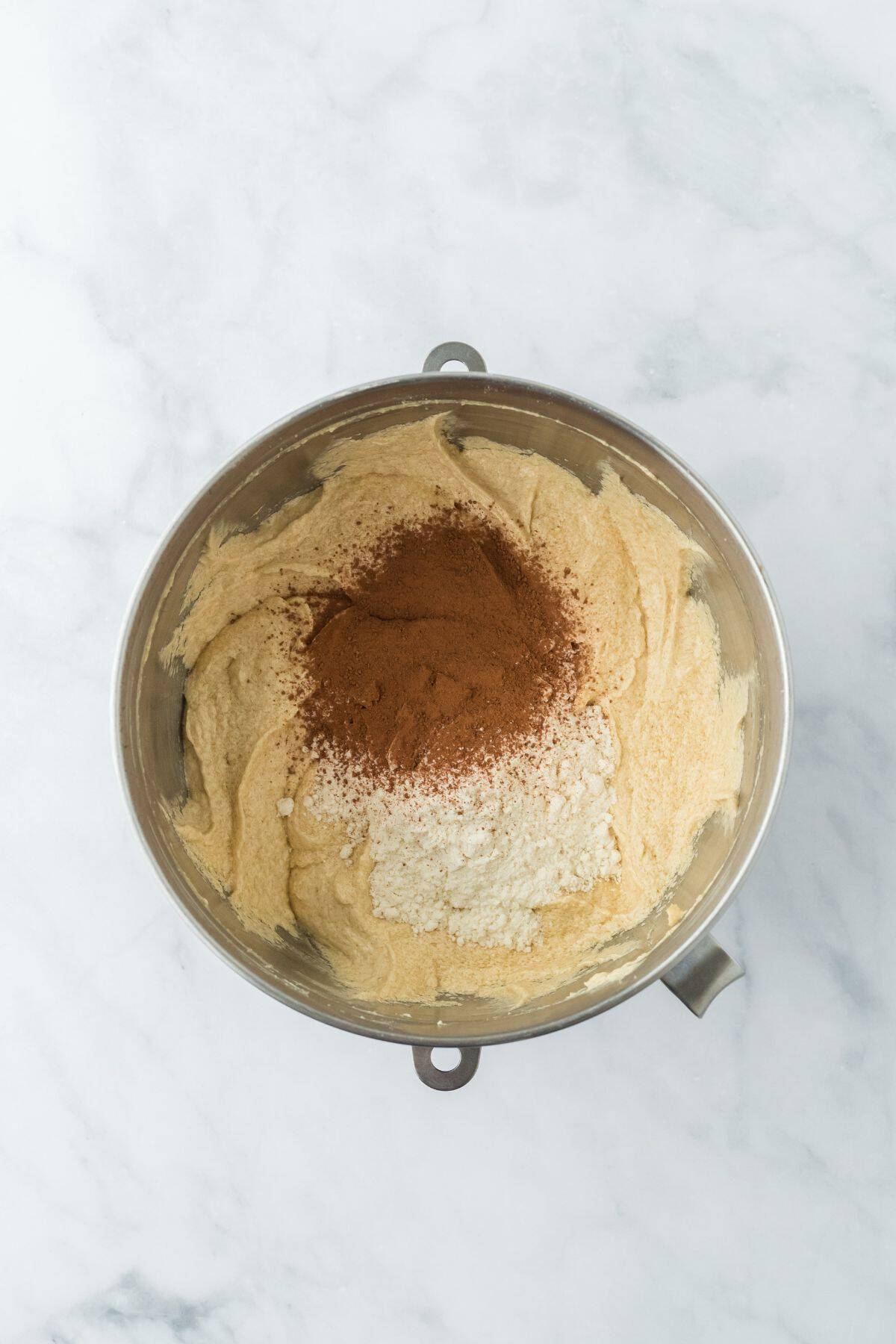 Cocoa powder and flour mixture added on top of batter in a metal mixing bowl