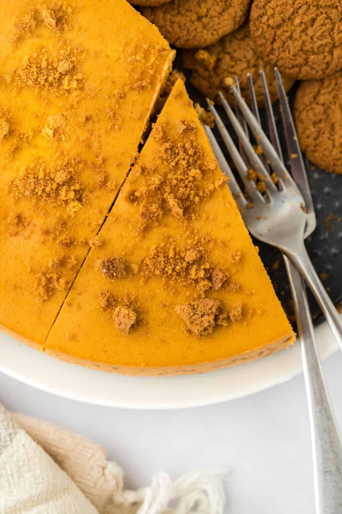 Overhead view of a partially sliced pumpkin cheesecake topped with crushed gingersnaps, with two forks nearby