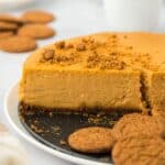 A pumpkin cheesecake with a missing slice, showing its smooth texture, surrounded by gingersnap cookies