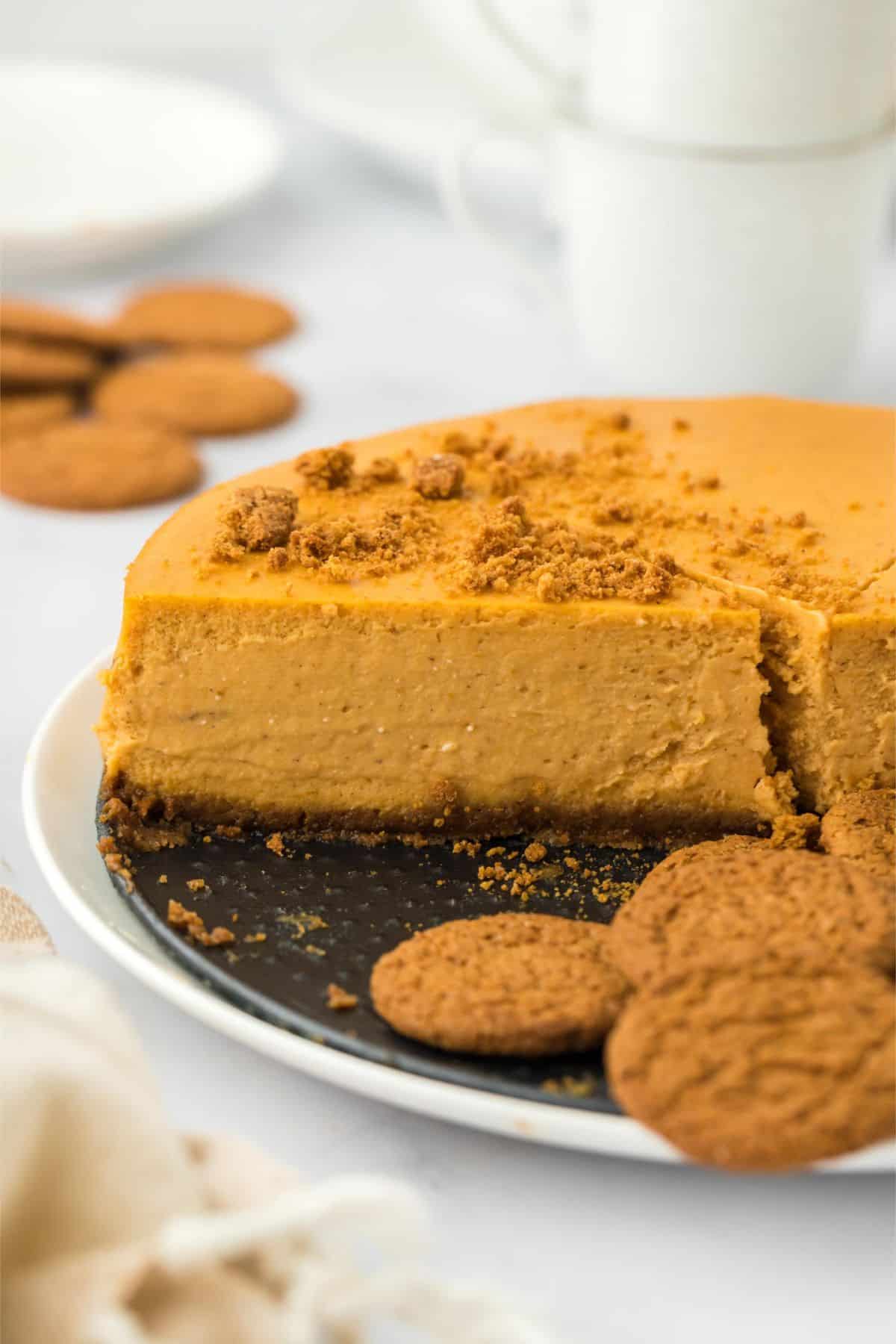 A pumpkin cheesecake with a missing slice, showing its smooth texture, surrounded by gingersnap cookies