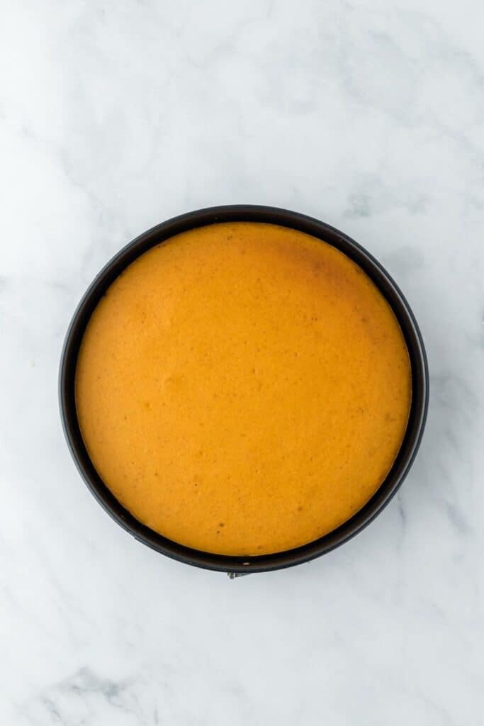A round, smooth pumpkin cheesecake in a springform pan, freshly baked