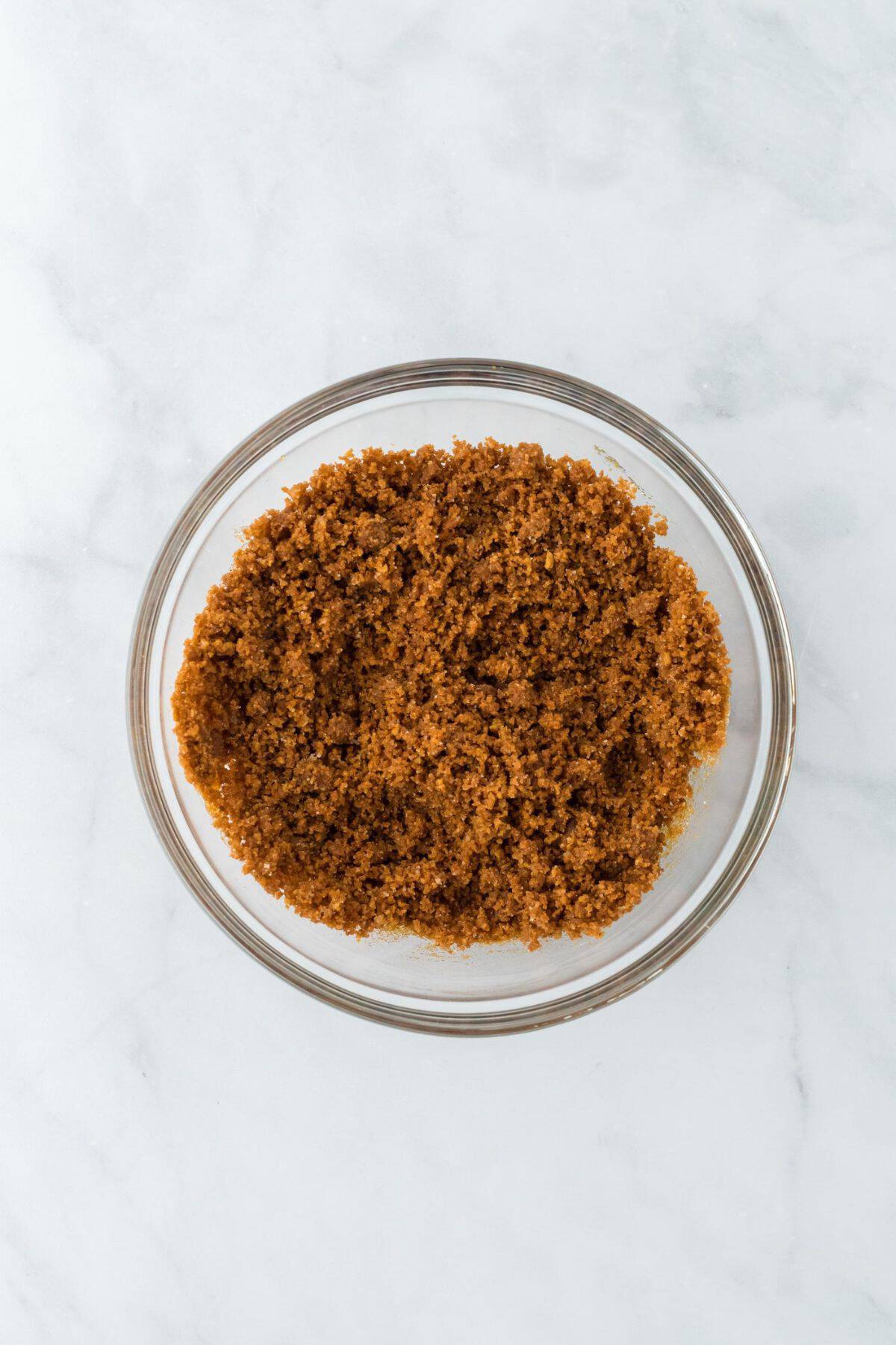 A mixture of gingersnap crumbs, sugar, and butter combined in a glass bowl, forming the crust mixture