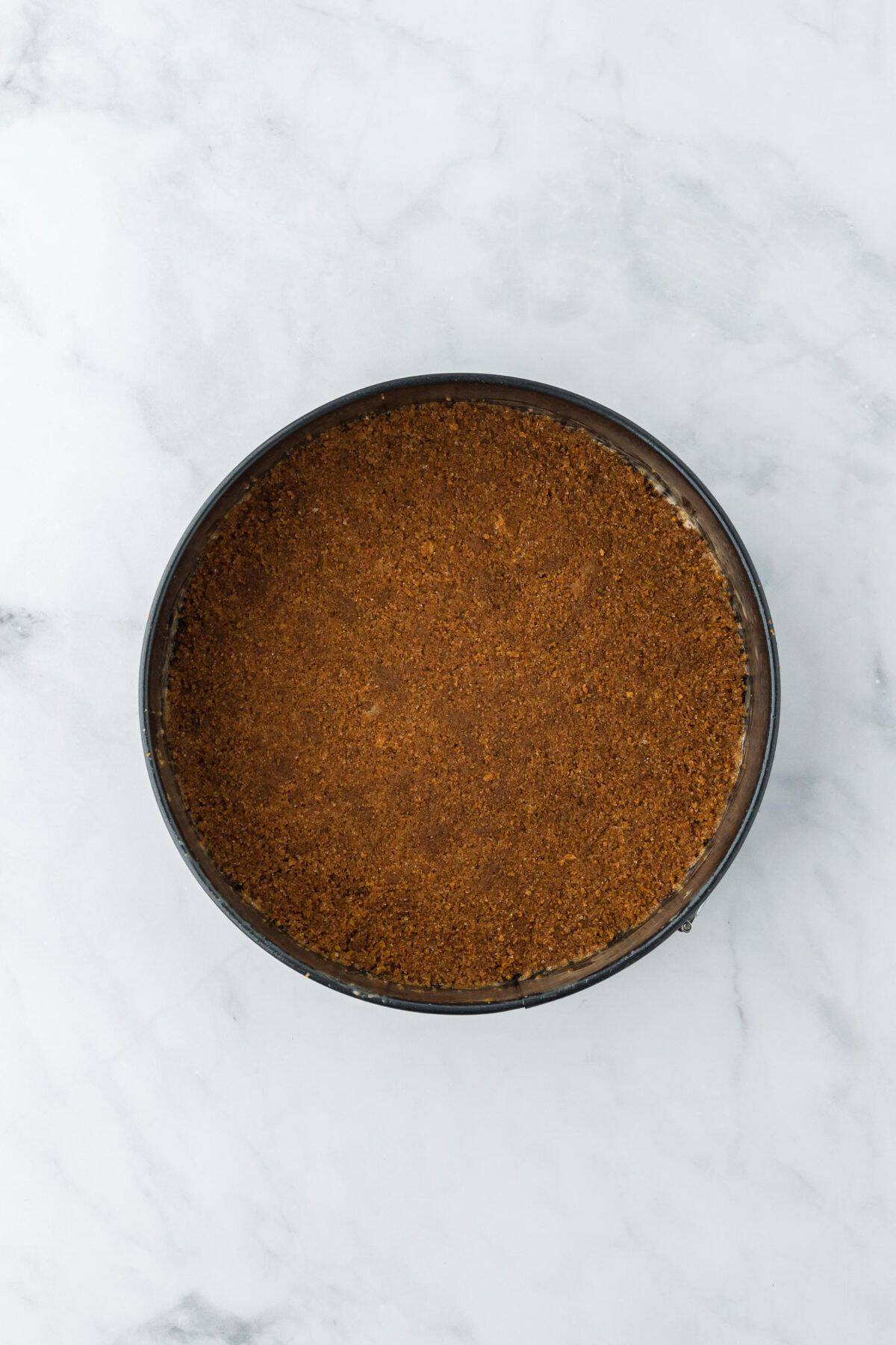 A smooth, evenly pressed gingersnap crust inside a round cake pan