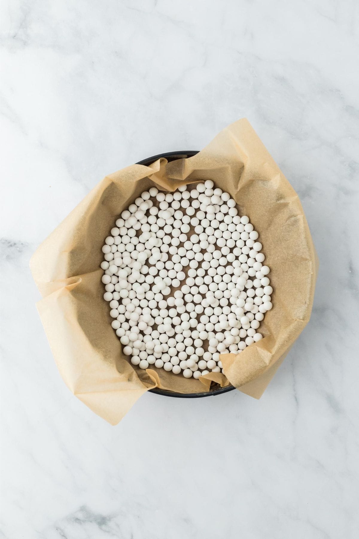 A crust lined with parchment paper and topped with ceramic pie weights inside a baking dish