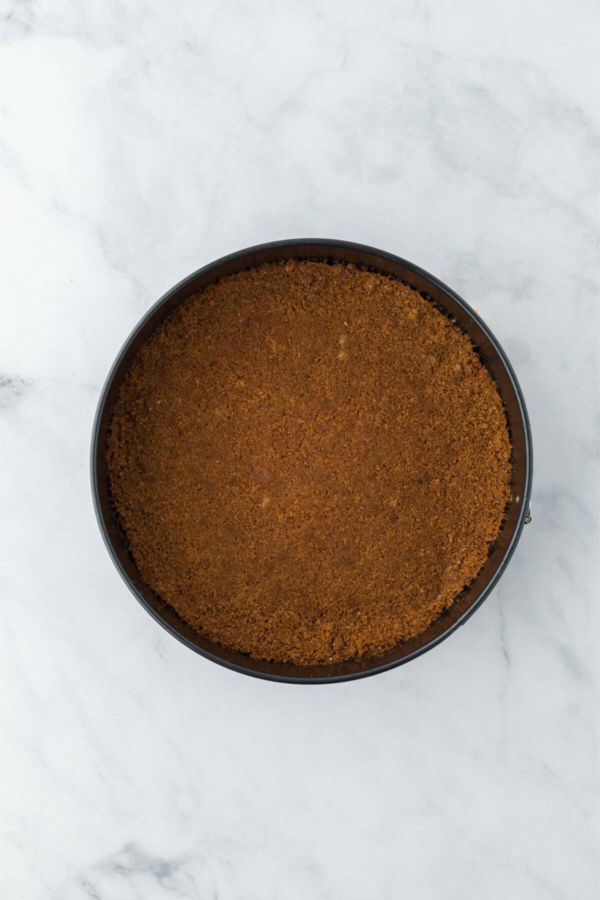 A finished crust pressed neatly into a round springform pan, ready for filling