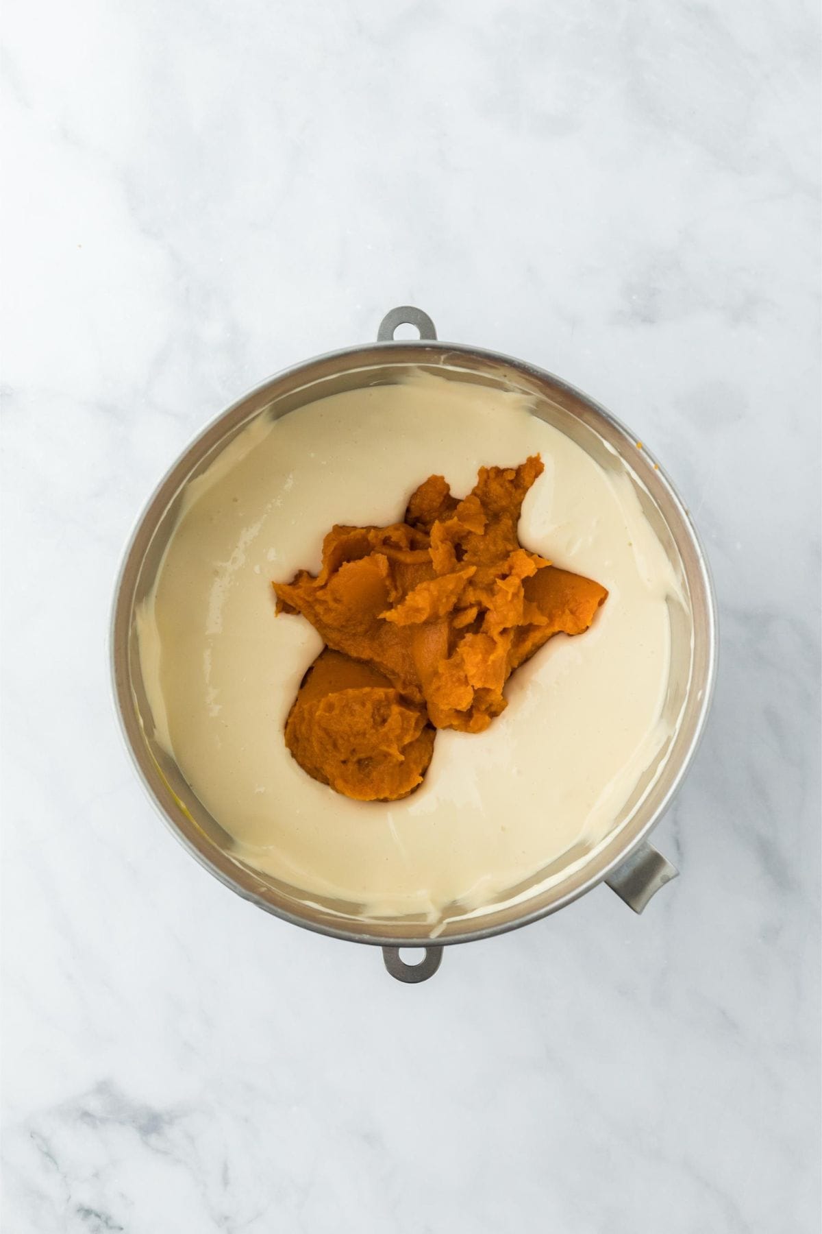 A large dollop of pumpkin puree added to the creamy cheesecake mixture in the mixing bowl