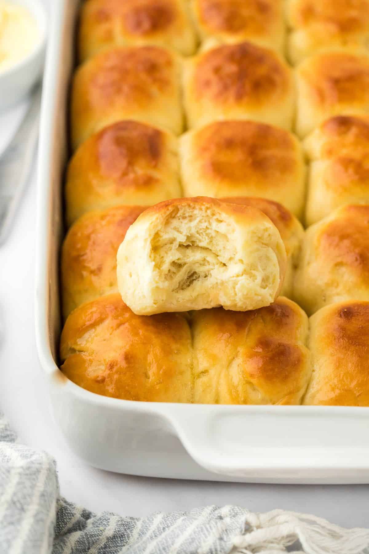 Closeup shot of a golden-brown yeast roll with a bite taken out of it, showing the soft, fluffy interior