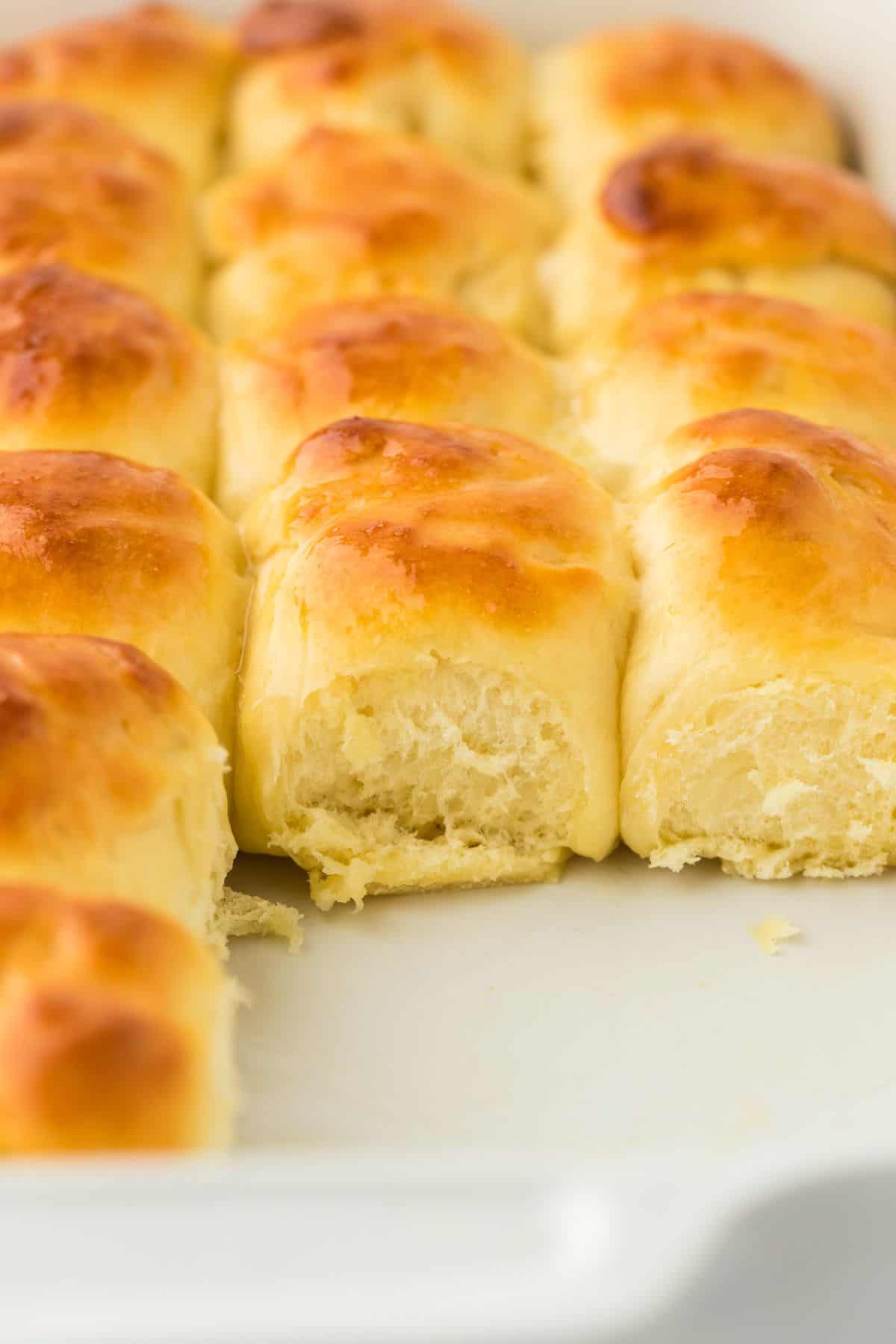 Close-up of soft, golden-brown yeast rolls in a baking dish, one missing from the corner