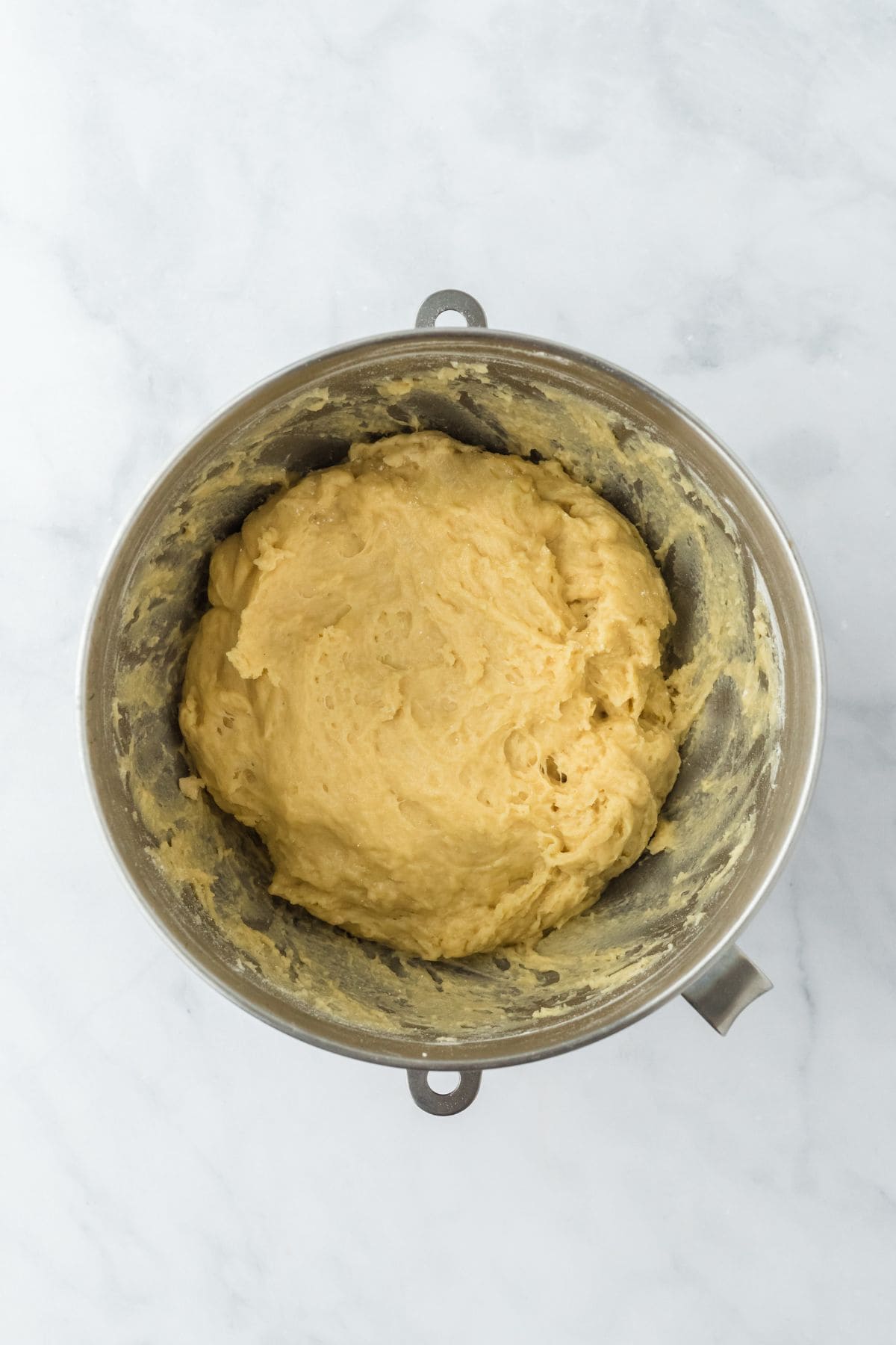 A metal mixing bowl with the dough beginning to smooth out after further mixing