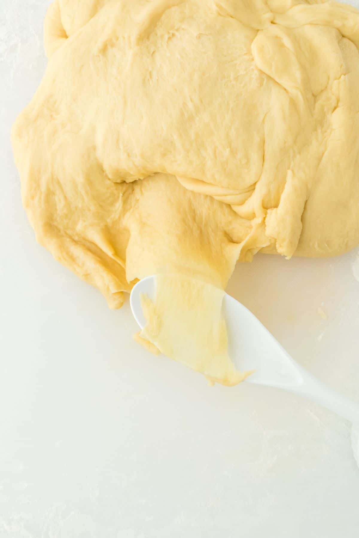 Soft dough being stretched with a spoon to show texture on a white surface